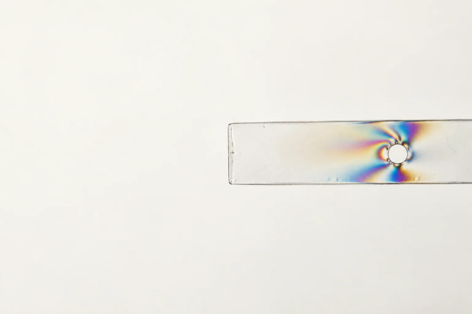 A clear acrylic strip reveals a small concentration of colour around a single stress point.